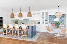 a kitchen with white cabinets and blue island in front of an oven, dining room table surrounded by wicker chairs