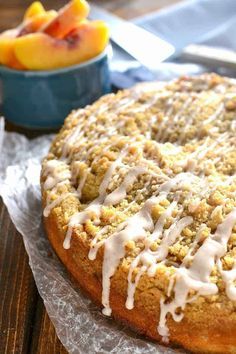 a cake with white icing sitting on top of a wooden table next to a bowl of peaches