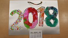 a paper calendar with the numbers 2013 and decorated in colorful beads on it, sitting on top of a wooden table