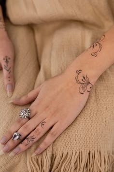 a woman's hand with tattoos on it sitting on a tan blanket next to a ring