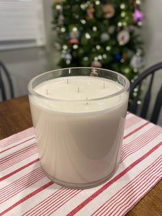 a white candle sitting on top of a table next to a christmas tree in the background