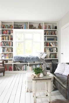 a living room filled with furniture and bookshelves next to a white floor covered in lots of books