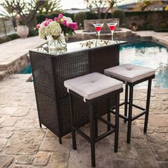 an outdoor bar with two stools next to a pool and flowers in a vase