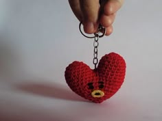 a hand holding a red knitted heart keychain with a bear face on it