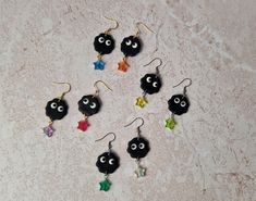 six pairs of black earrings with colorful stars and eyes are shown on a white surface