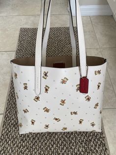 COACH HIGHLINE TOTE WITH BEAR PRINT CHALK/MULTI COLOR CROSSGRAIN LEATHER OPEN BAG WITH LARGE COMPARTMENT LINED IN LIGHT TAN SUEDE COACH CREED PATCH C6590 DOUBLE HANDLES 9 3/4" DROP COACH RED LEATHER EMBOSSED HANGTAG BAG IS COVERED IN THE CUTEST LITTLE BEAR PRINT WITH MULTI COLORED OUTFITS SOME WITH GLITTER HIGHLIGHTS 14 1/4"W AT THE WIDEST POINT X 12 1/4"H X 4 1/4"D CONDITION - BRAND NEW WITH SALES TAG ATTACHED, IF YOU LIKE LITTLE BEARS YOU WILL LOVE THIS CUTE BAG! THANK YOU White Textured Leather Travel Bags, Designer White Textured Leather Bags, White Textured Leather Shopping Bag, White Textured Leather Bags For On-the-go, White Textured Leather Bag For Errands, White Textured Leather Coach Bag, Coach White Textured Leather Bag, White Textured Leather Shoulder Bag For Errands, Multi Colored Outfit