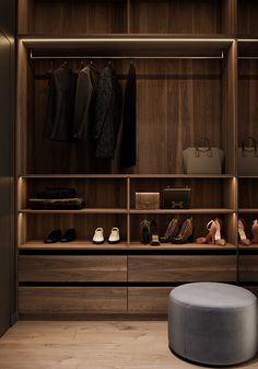 a walk in closet with shoes and handbags on the shelves, along with an ottoman