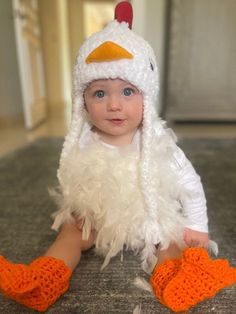 a baby in a chicken costume sitting on the floor wearing orange crocheted shoes