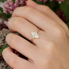 a woman's hand wearing a gold ring with a diamond on it and flowers in the background