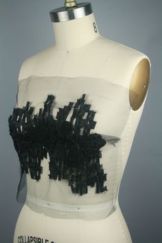 a mannequin with black flowers on it's chest and back, in front of a gray background