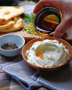 a person is pouring olive oil into a bowl of hummus and pita bread