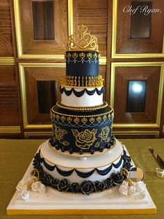 a three tiered cake is decorated with black and gold designs on the top layer