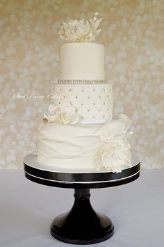 a three tiered wedding cake with white flowers and pearls on the top is sitting on a black stand