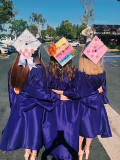 three girls in purple graduation gowns and hats walk down the street with their arms around each other