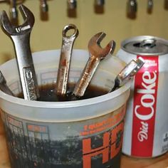 a cup filled with lots of wrenches sitting next to a can of coca - cola