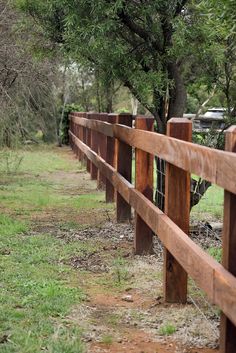 a wooden fence in the middle of a grassy area with trees and grass on both sides