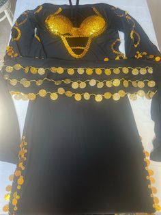 a black dress with gold sequins on the shoulders and long sleeves is displayed