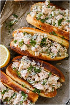 several breads with chicken salad on them and lemon wedges next to each other