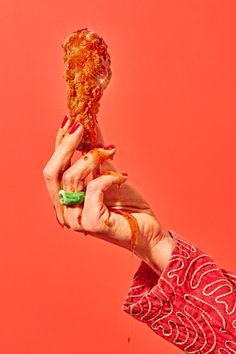 two hands holding up a piece of food on top of a pink background with red and green designs