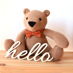 a brown teddy bear sitting on top of a wooden table next to the word hello