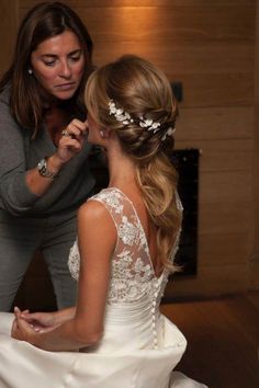 a woman helping another woman put on her wedding dress in front of a fireplace with lights