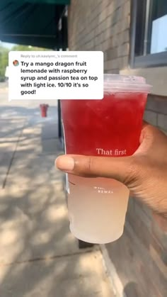 a person holding up a cup with red liquid in it on the side of a building