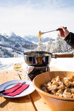 a bowl of food on top of a wooden table next to a glass of wine