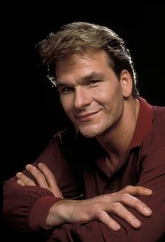 a close up of a person wearing a red shirt with his arms crossed and smiling