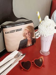 a red table topped with sunglasses and a purse next to a cup filled with whipped cream