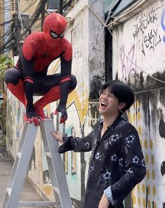 a man standing on top of a ladder next to a spiderman statue