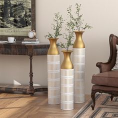 three gold vases sitting on top of a hard wood floor next to a chair