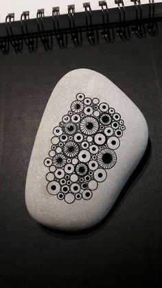 a white rock with black circles on it and a spiral design painted on the stone