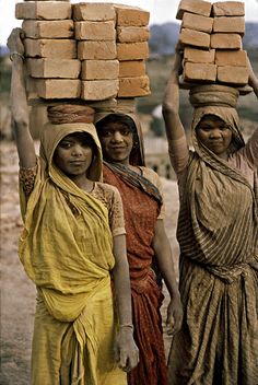 three women carrying bricks on their heads