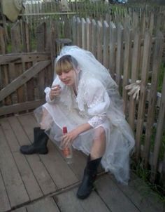 a woman in white dress and black boots sitting on wooden floor next to wood fence