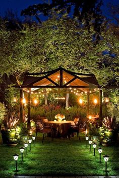 an outdoor gazebo with lights on it in the middle of some grass and trees