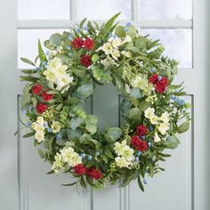 a wreath with red, white and blue flowers is hanging on the front door window