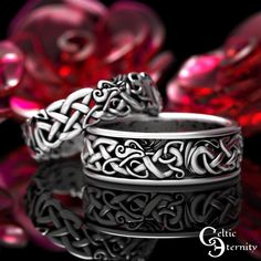 two wedding rings sitting next to each other on top of a black surface with pink flowers