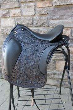 a black horse saddle sitting on top of a metal stand next to a brick wall