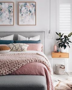 a bed with pink and grey sheets in a bedroom next to two pictures on the wall