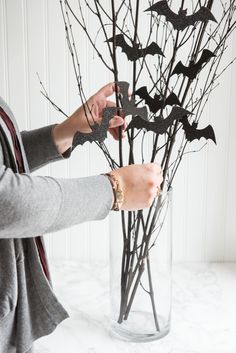 a woman arranging branches with bats in a vase