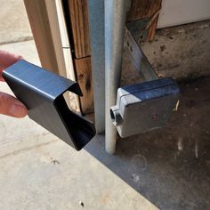 a hand holding an open door handle near a metal pole with a wooden door in the background