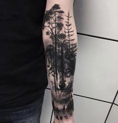 a man's arm with a wolf and pine trees tattoo on the left forearm