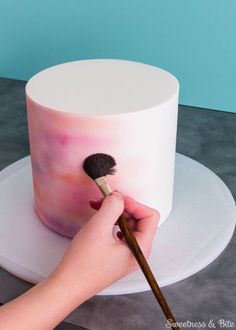 a person painting a pink and white cake with a brush