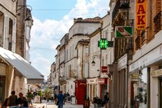 people are walking down the street in an old european city with shops and restaurants on both sides