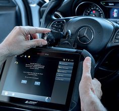 a man is holding an electronic device in his hand and driving the car with it's steering wheel