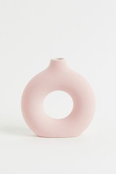 a light pink vase sitting on top of a white table next to a black object