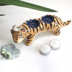 a ceramic tiger figurine next to some rocks and candles on a white surface