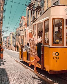 a woman standing on the side of a trolley car with her arms in the air