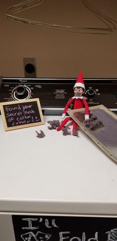 an elf sitting on top of a dryer next to a chalkboard with writing on it