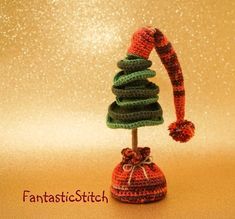 a crocheted christmas tree with a hat on it's head, sitting in front of a gold background